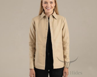 May include: A tan leather shirt with long sleeves and a button-down front. The shirt has a collared neckline and is worn over a black top and black trousers. The shirt is a neutral colour and appears to be made of soft leather.