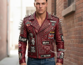 Könnte beinhalten: Burgunderfarbene Lederjacke mit silbernen Stacheln an Schultern und Kragen. Die Jacke hat Aufnäher mit Bandnamen und Punkrock-Symbolen, darunter "The Clash" und "Ramones". Die Jacke ist mit silbernen Nieten besetzt und hat einen Reißverschluss.