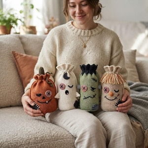 May include: Four small, knitted drawstring pouches featuring Halloween-themed designs: a burnt orange pumpkin, a white ghost with a black moon, a green monster with bolts, and a beige scarecrow with yarn hair, all with button eyes and stitched mouths.