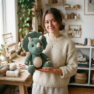 May include: A green knitted triceratops toy with a large frill, three horns, and a cream-colored belly patch. The dinosaur has dark brown eyes and is crafted with a textured yarn finish, featuring small claws on its feet and hands.