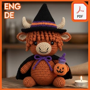 May include: A crocheted Highland cow doll in orange, brown, and black, wearing a witch hat and cape, holding a pumpkin. The hat has purple and orange stripes. The doll has tan horns and ears. The image includes the text "ENG DE" and a PDF icon.