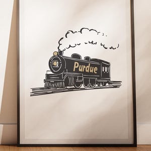 Op de afbeelding: Zwart-wit ingelijste print met een illustratie van een vintage trein. De trein, met het opschrift "Purdue", stoot rook uit. Een cirkelvormig logo linksboven toont "Dorm Rooms of Purdue".