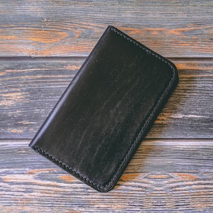 May include: A black leather wallet with a stitched edge, lying on a wooden surface.
