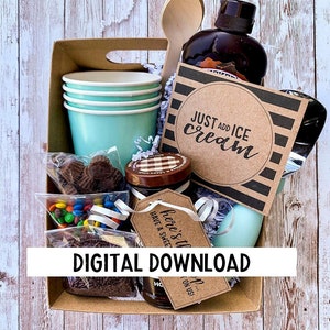 May include: A brown cardboard gift basket filled with a variety of items, including a bottle of chocolate sauce, a wooden spoon, a small jar of chocolate sprinkles, a bag of colourful sweets, a bag of chocolate chips, a stack of light blue paper cups, and a brown card with the text "JUST ADD ICE CREAM".