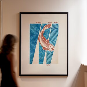 May include: Framed art print featuring a stylized salmon illustration in shades of red and white, set against a blue patterned background. The print includes the text "Tsukiji Outer Market Tokyo". The artwork is displayed in a black frame.