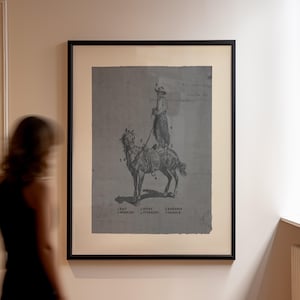 May include: A framed print featuring a grey-toned illustration of a person standing on a horse. The artwork includes numbered labels for gear, with text at the bottom reading: 1 HAT, 2 SPURS, 3 HARNESS, 4 WOOLIES, 5 STIRRUPS, 6 SADDLE. The print is in a black frame.