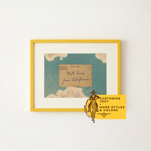 May include: A framed print with a yellow border. The print features a vintage postcard design with a blue sky and cloud background. The postcard reads "With love, from California."