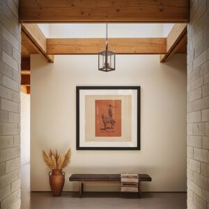 May include: A hallway featuring a dark wood bench with a patterned throw, a terracotta vase filled with dried pampas grass, and a framed square print of a person on a horse. A metal lantern hangs from exposed wooden ceiling beams above.