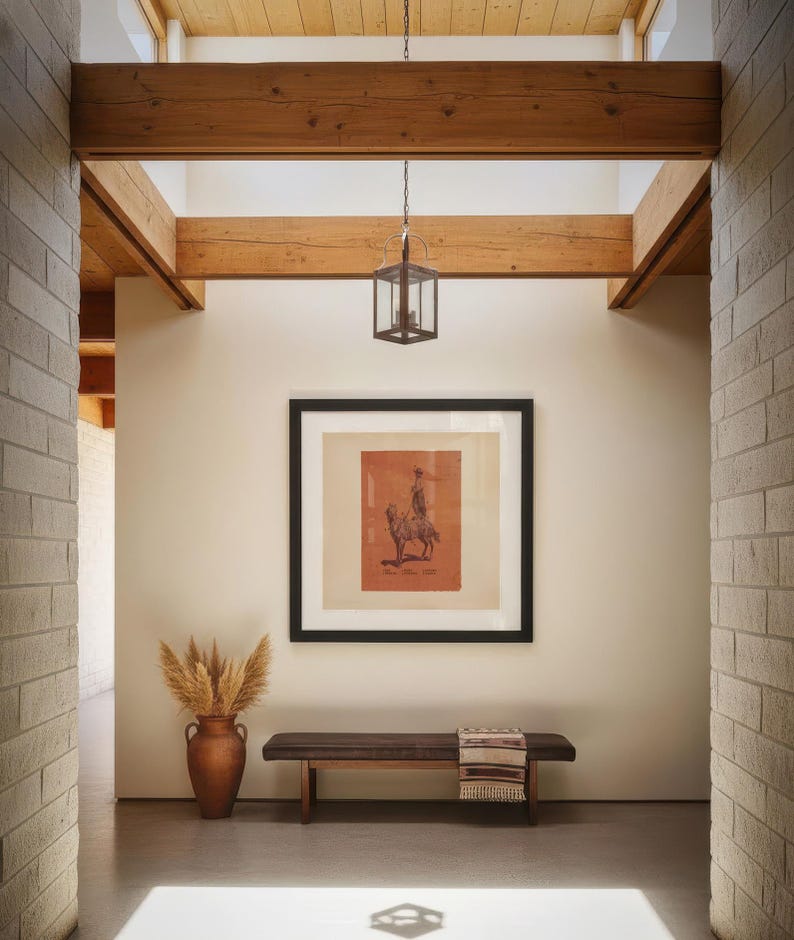 May include: A hallway featuring a dark wood bench with a patterned throw, a terracotta vase filled with dried pampas grass, and a framed square print of a person on a horse. A metal lantern hangs from exposed wooden ceiling beams above.