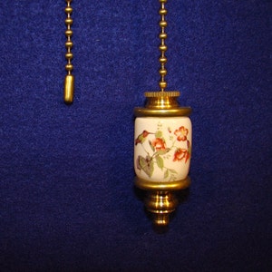 May include: A gold chain with a porcelain pull chain with a hummingbird and floral design. The pull chain is white with red and green accents.