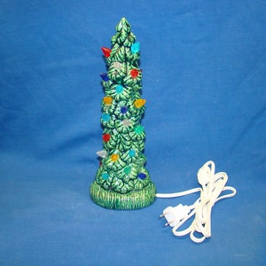 May include: A green ceramic Christmas tree with multi-colored lights. The tree is plugged in and has a white cord.