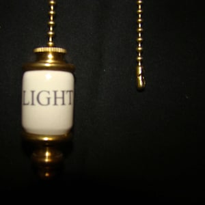 May include: A gold light pull with a white ceramic cylinder that says "LIGHT" on it.