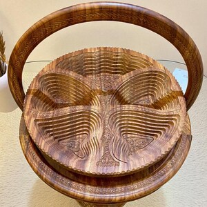 May include: A finely crafted wooden basket with a folding design. The basket has detailed carvings and a large handle. The natural wood colour and intricate carvings give it a rustic and elegant appearance. The basket is designed to expand and contract.