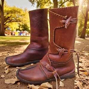 Puede incluir: Un par de botas de cuero marrón con un diseño medieval. Las botas tienen una caña alta, costuras decorativas y cordones de cuero. Están hechas de cuero marrón oscuro y son adecuadas para cosplay o recreaciones históricas.