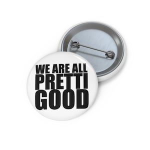 May include: Two white round badges with a pin back. The front badge has the text "WE ARE ALL PRETTI GOOD" in bold black letters. The second badge is partially visible.