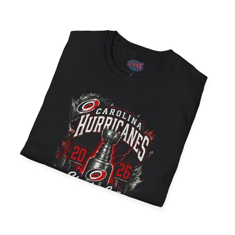 May include: A black t-shirt featuring a graphic print of the Carolina Hurricanes logo and a trophy. The design includes the text 'CAROLINA HURRICANES' in white, the numbers '20' and '26' in red, and a small 'JENNX' logo printed on the inside neck label.