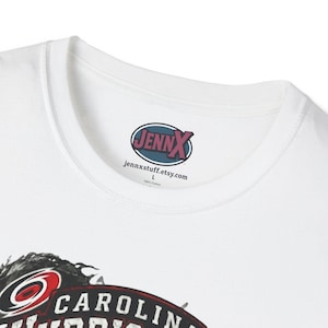 May include: A white t-shirt featuring a crew neckline and a printed inner label that reads JENNX, jennxstuff.etsy.com, L, and 100% Cotton. The lower portion of the shirt displays a partial graphic with the text CAROLINA in bold white letters.