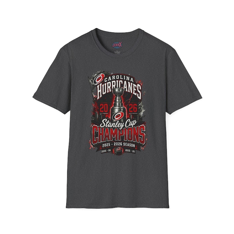 May include: A dark gray short-sleeve t-shirt featuring a graphic of the Stanley Cup with the text Carolina Hurricanes Stanley Cup Champions 2025-2026 Season. The design includes red and white accents, a hockey puck, and the team logo.
