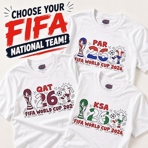 May include: Three white t-shirts featuring FIFA World Cup 2026 graphics. Each shirt displays a trophy, the number 26, a soccer player, and country codes QAT, PAR, or KSA. The text CHOOSE YOUR FIFA NATIONAL TEAM! appears above the shirts.