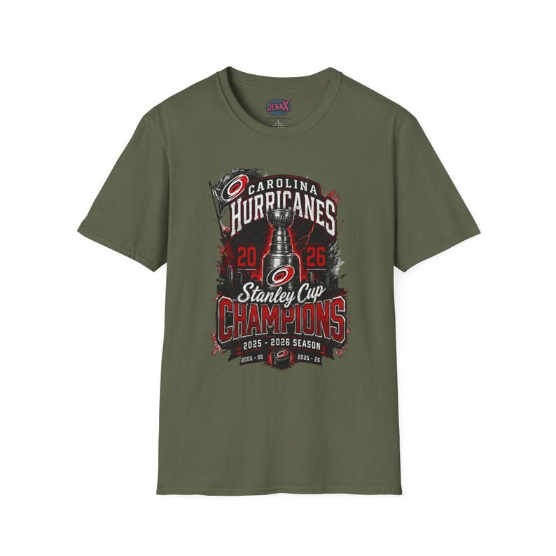 May include: An olive green short-sleeve t-shirt featuring a graphic print of the Carolina Hurricanes Stanley Cup Champions 2025-2026 season. The design includes the team logo, a trophy illustration, and the text 2025-2026 season and 2005-06.