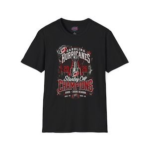 May include: A black short-sleeve t-shirt featuring a graphic of the Stanley Cup trophy, the Carolina Hurricanes logo, and text reading Carolina Hurricanes Stanley Cup Champions 2025-2026 Season, with additional dates 2005-06 and 2025-26.