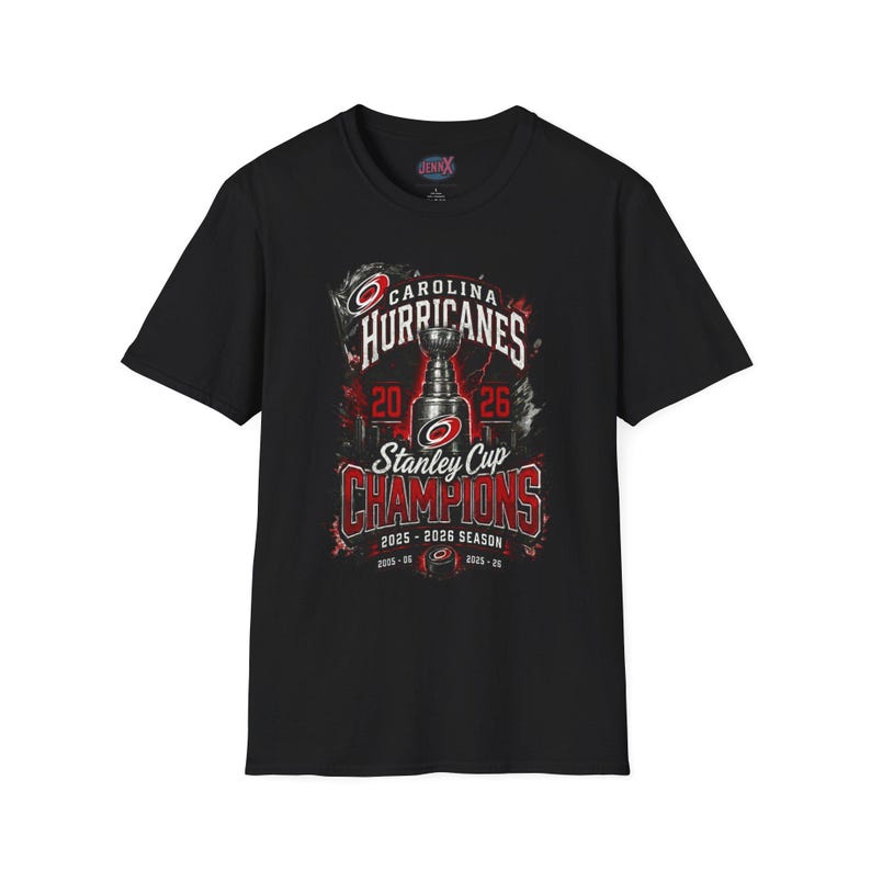 May include: A black short-sleeve t-shirt featuring a graphic of the Stanley Cup trophy, the Carolina Hurricanes logo, and text reading Carolina Hurricanes Stanley Cup Champions 2025-2026 Season, with additional dates 2005-06 and 2025-26.