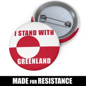 May include: A round button featuring the Greenlandic flag design, with the text "I STAND WITH GREENLAND" in red. The words "MADE FOR RESISTANCE" are printed below the button in a bold font.