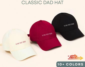 May include: Three custom printed classic dad hats in cream, burgundy, and black. Each hat features the text "YOUR TEXT HERE" in a contrasting color. The image also includes text that says "CUSTOM PRINTED CLASSIC DAD HAT" and "10+ COLORS".