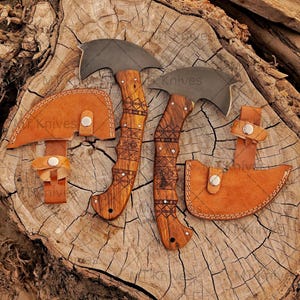 May include: Two hatchets with curved blades and wooden handles with etched designs, accompanied by leather sheaths. The hatchets and sheaths are displayed on a textured wooden surface. The text "Mk Knives" is visible on the sheaths.