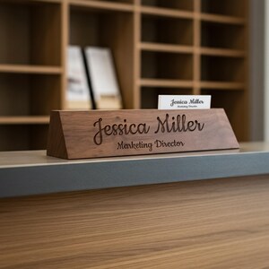 Puede incluir: Un letrero de escritorio de madera con el nombre "Jessica Miller" y el t&iacute;tulo "Marketing Director" grabados. Una tarjeta de visita con el mismo nombre est&aacute; colocada encima. El letrero es de madera oscura.