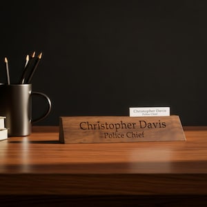 Puede incluir: Un letrero de escritorio de madera con el nombre "Christopher Davis" grabado y el t&iacute;tulo "Police Chief". Tambi&eacute;n se ve una tarjeta de presentaci&oacute;n m&aacute;s peque&ntilde;a y una taza con l&aacute;pices.