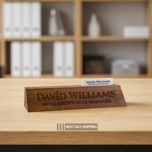 Puede incluir: Un letrero de escritorio de madera con el nombre grabado "DAVID WILLIAMS" y el t&iacute;tulo "HUMAN RESOURCES MANAGER". Una tarjeta de visita con el mismo nombre y t&iacute;tulo est&aacute; en la ranura. El letrero est&aacute; sobre un escritorio de madera.
