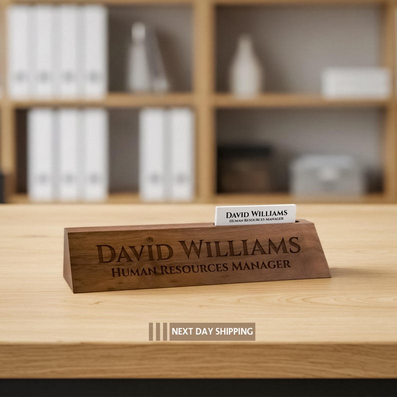 Puede incluir: Un letrero de escritorio de madera con el nombre grabado "DAVID WILLIAMS" y el t&iacute;tulo "HUMAN RESOURCES MANAGER". Una tarjeta de visita con el mismo nombre y t&iacute;tulo est&aacute; en la ranura. El letrero est&aacute; sobre un escritorio de madera.