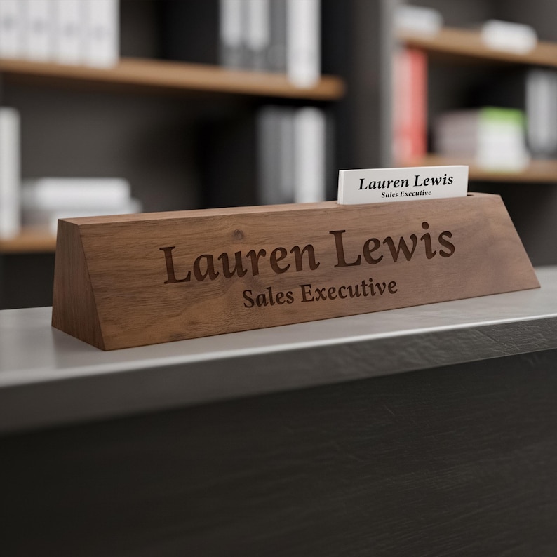 Puede incluir: Un letrero de escritorio de madera con el nombre "Lauren Lewis" y el t&iacute;tulo "Sales Executive" grabados. Una tarjeta de visita con el mismo nombre y t&iacute;tulo est&aacute; en una ranura. El letrero es de madera oscura.