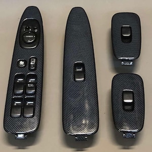 Könnte beinhalten: Ein Satz von fünf schwarzen Innenraum-Bedienfeldern für Autos mit Kohlefaserstruktur. Die Paneele umfassen Bedienelemente für Spiegel, Fenster und Türschlösser. Die Paneele haben eine glänzende Oberfläche.