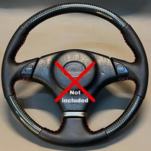 Könnte beinhalten: Ein schwarzes Autolenkrad mit Carbonfaser-Akzenten und roten Nähten. Das Lenkrad hat einen perforierten Ledergriff und zwei "DOWN"-Tasten. Die Mitte ist mit einem roten "X" und den Worten "Not included" markiert.