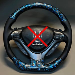 May include: A black steering wheel with blue and black accents. The center of the wheel has a red "Not included" symbol over the Honda logo. The wheel has buttons for cruise control, volume, and other functions.