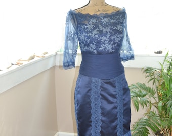 May include: A blue lace dress with a satin skirt and a lace overlay. The dress has a fitted bodice and a high neckline. The dress is on a mannequin.