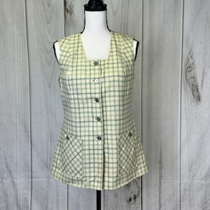 May include: A sleeveless, button-up vest with a plaid pattern in shades of green and cream. The vest has two pockets on the front and a slightly flared hem.