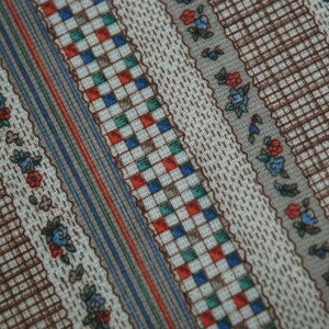 May include: A close-up of a fabric with a repeating pattern of brown, blue, red, and green stripes. The fabric has a checkered pattern in the center of the stripes.