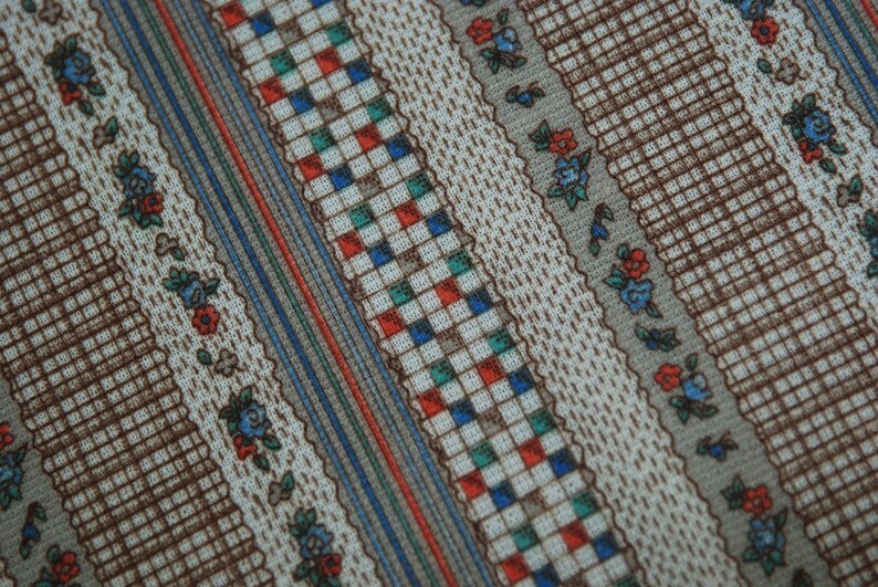 May include: A close-up of a fabric with a repeating pattern of brown, blue, red, and green stripes. The fabric has a checkered pattern in the center of the stripes.