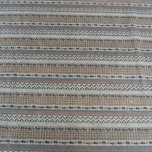 May include: A white fabric with a repeating pattern of brown, blue, and red stripes. The stripes are made up of small squares and other geometric shapes.