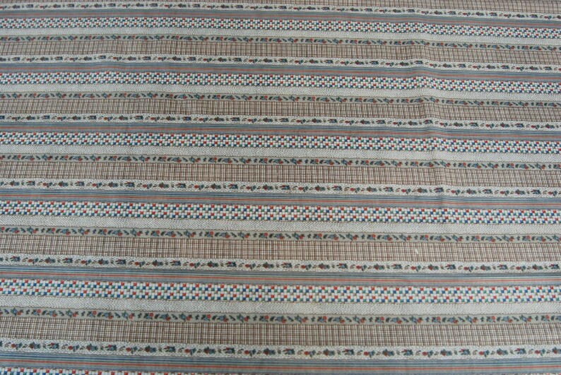 May include: A white fabric with a repeating pattern of brown, blue, and red stripes. The stripes are made up of small squares and other geometric shapes.