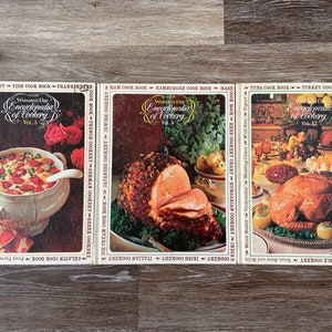 May include: Three vintage cookbooks with colorful covers featuring food illustrations. The titles are "Woman's Day Encyclopedia of Cookery" with volumes 5, 6, and 12.