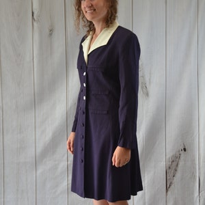May include: A long-sleeved dress with a white collar and button closure. The dress is a dark purple color and has a slightly flared skirt.