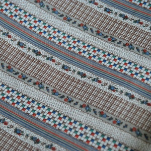 May include: Striped fabric with a brown, white, blue, red, and green pattern. The fabric has a small floral design.
