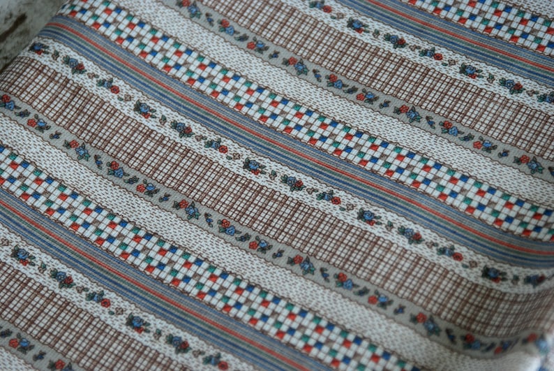 May include: Striped fabric with a brown, white, blue, red, and green pattern. The fabric has a small floral design.