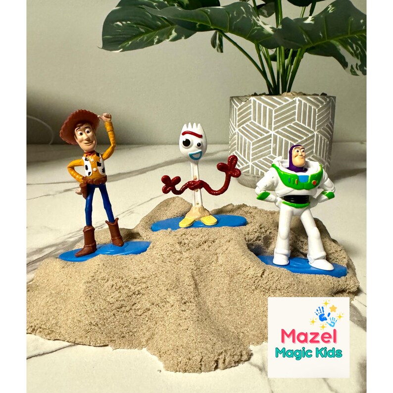 May include: Three Toy Story character figurines: Woody, Forky, and Buzz Lightyear, are displayed on a sandy surface with blue platforms. Woody is in a cowboy outfit, Forky is a white spork, and Buzz is in a spacesuit. A potted plant is in the background.