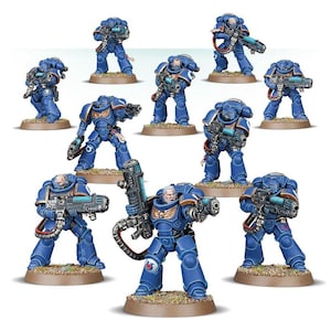 May include: A group of miniature blue Space Marine figures, each holding futuristic weapons. The figures are in dynamic poses, standing on small, textured bases. The armour has detailed features and metallic highlights.