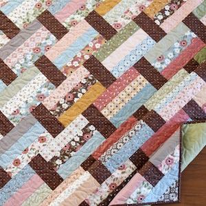 May include: A quilt with a brown, blue, pink, and green chevron pattern. The quilt is made of various floral and geometric patterned fabrics.
